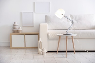 Photo of Stylish lamp on table and vases near sofa indoors