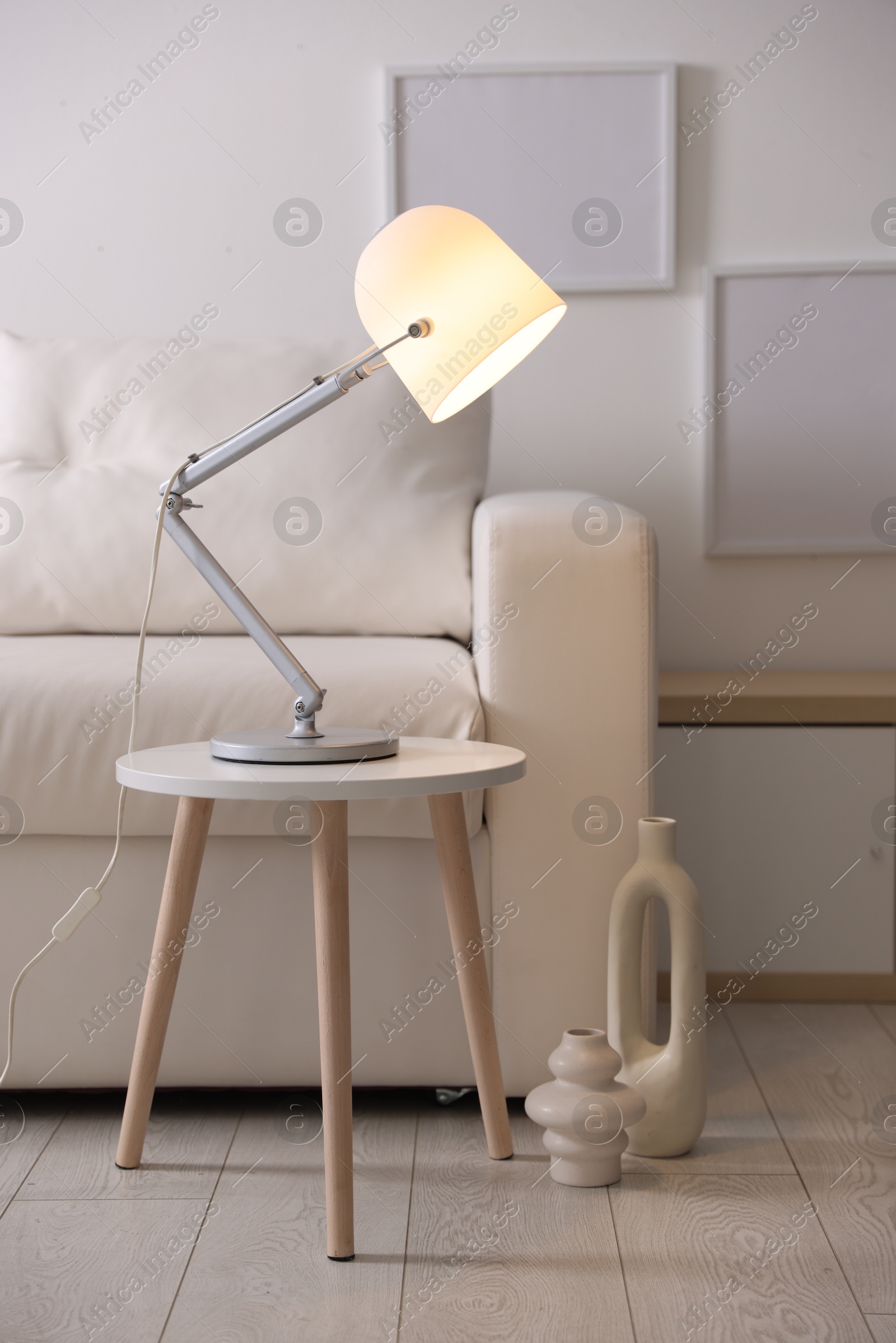 Photo of Stylish lamp on table and vases near sofa indoors