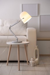 Photo of Stylish lamp on table and vases near sofa indoors