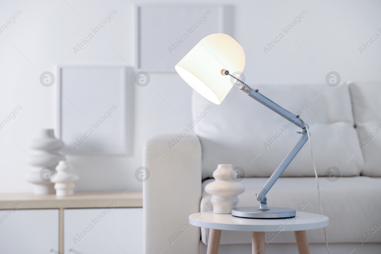 Photo of Stylish lamp and vase on table near sofa indoors, space for text