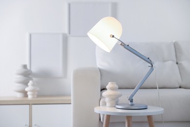 Photo of Stylish lamp and vase on table near sofa indoors, space for text