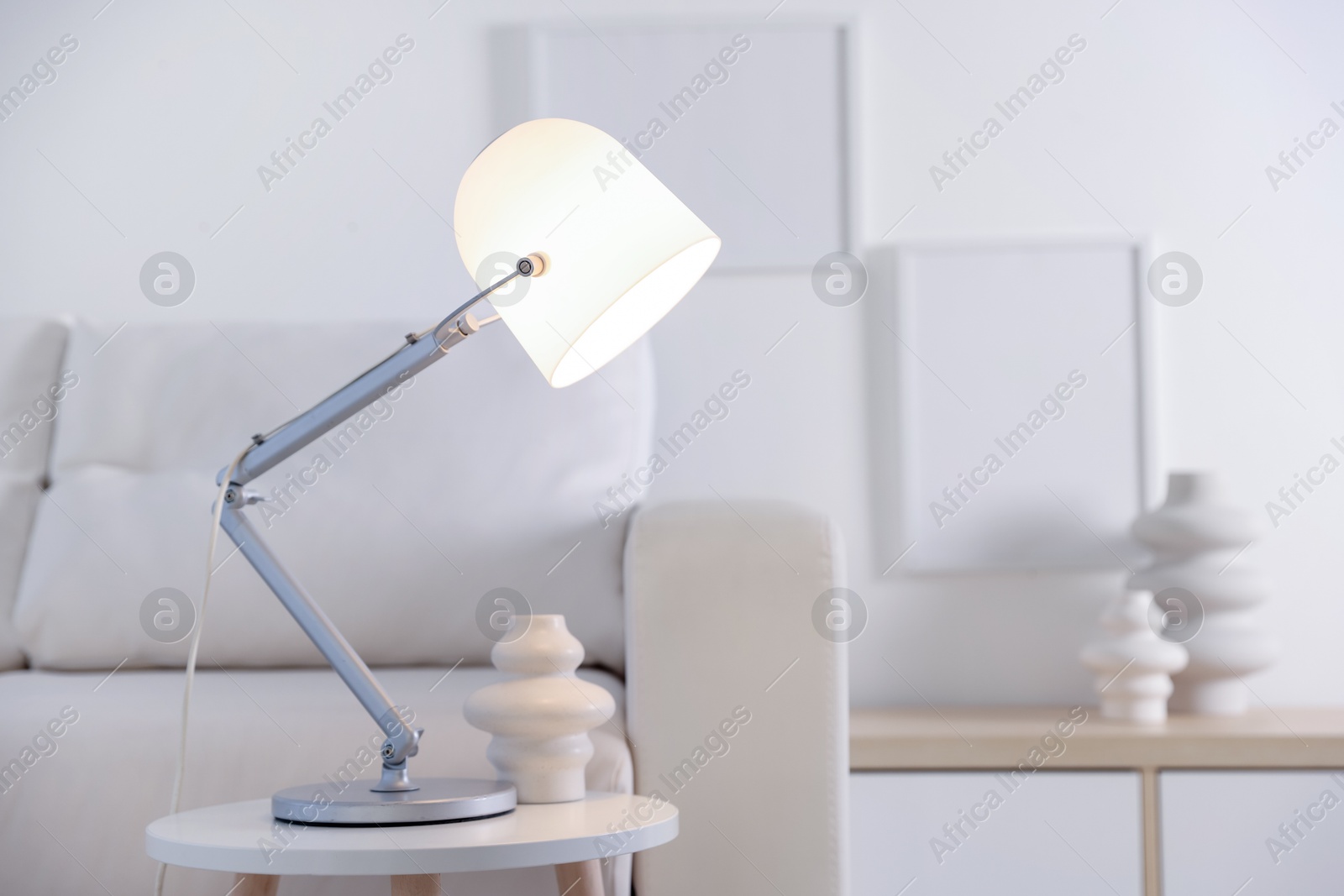 Photo of Stylish lamp and vase on table near sofa indoors, space for text