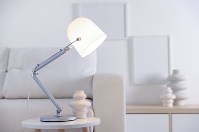 Photo of Stylish lamp and vase on table near sofa indoors, space for text