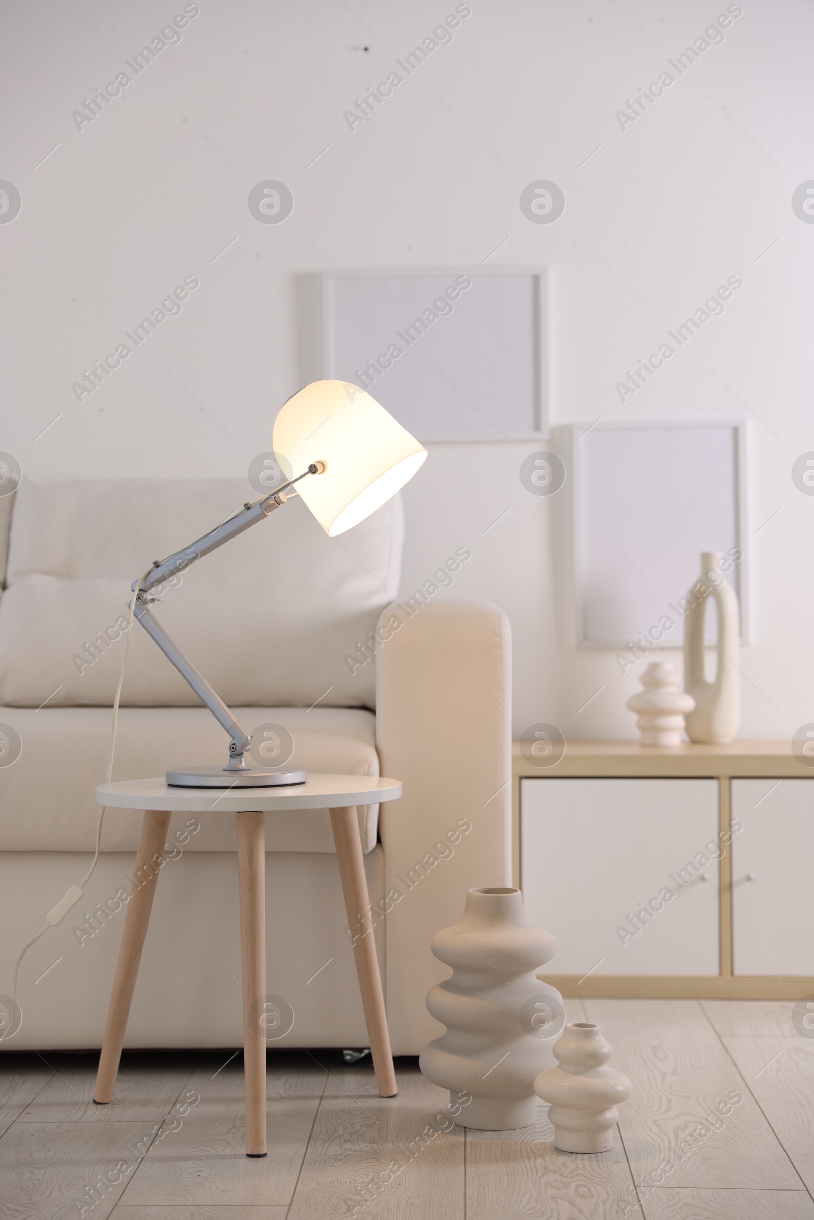 Photo of Stylish lamp on table and vases near sofa indoors