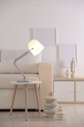 Photo of Stylish lamp on table and vases near sofa indoors