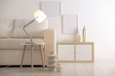 Photo of Stylish lamp on table and vases near sofa indoors