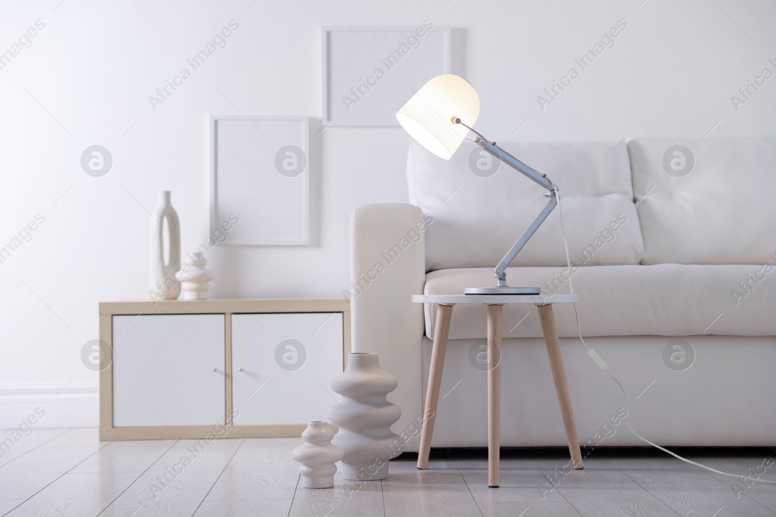 Photo of Stylish lamp on table and vases near sofa indoors