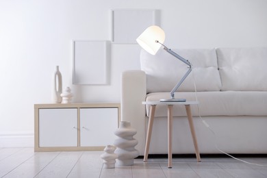 Photo of Stylish lamp on table and vases near sofa indoors