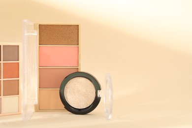 Photo of Eyeshadow palettes and pan on beige background with shadows, closeup. Space for text