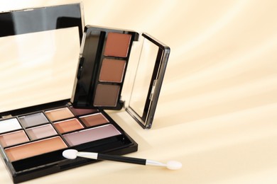 Photo of Eyeshadow palettes and applicator on beige background with shadows, closeup. Space for text