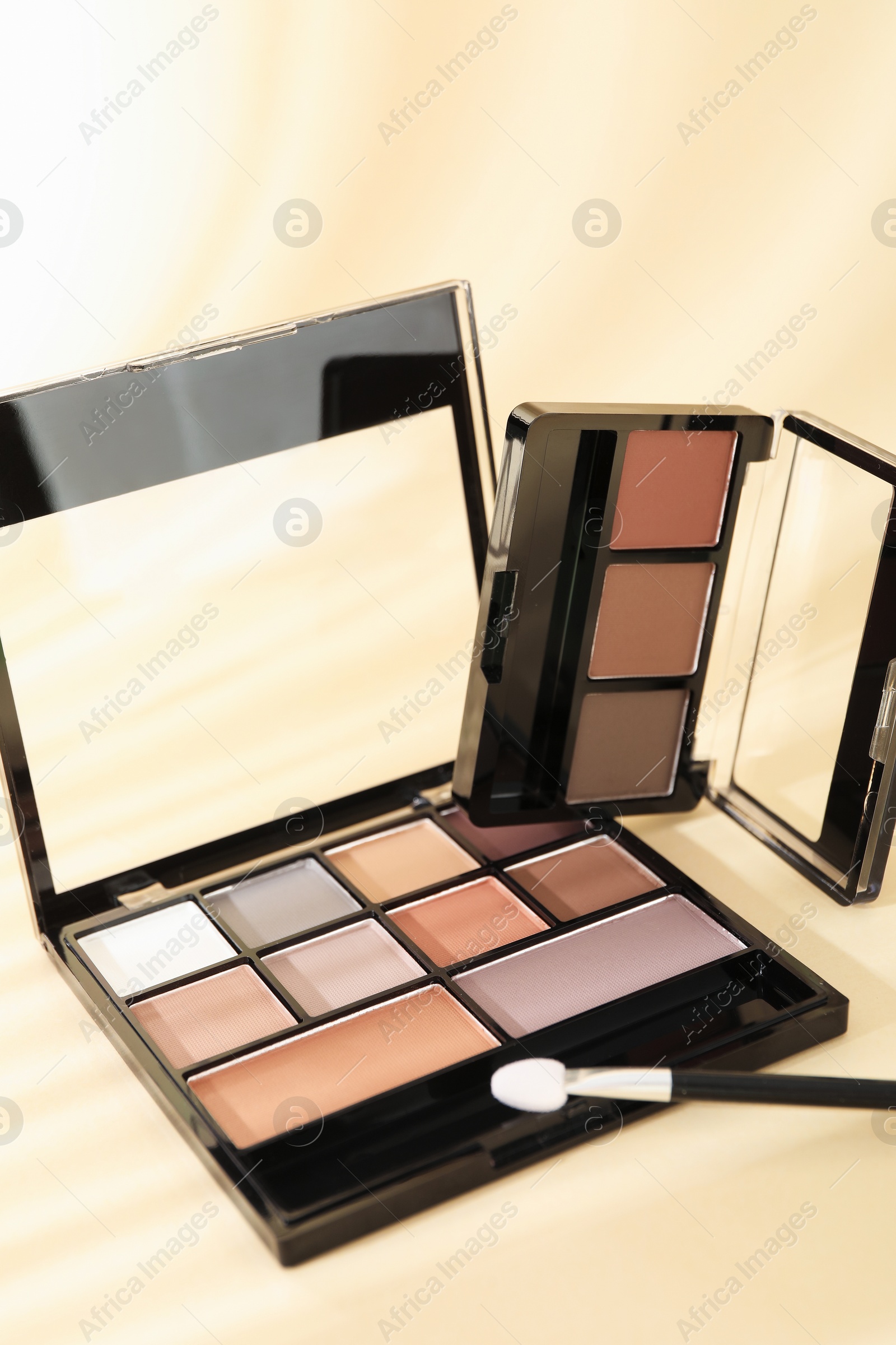Photo of Eyeshadow palettes and applicator on beige background with shadows, closeup