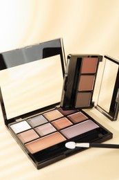 Photo of Eyeshadow palettes and applicator on beige background with shadows, closeup