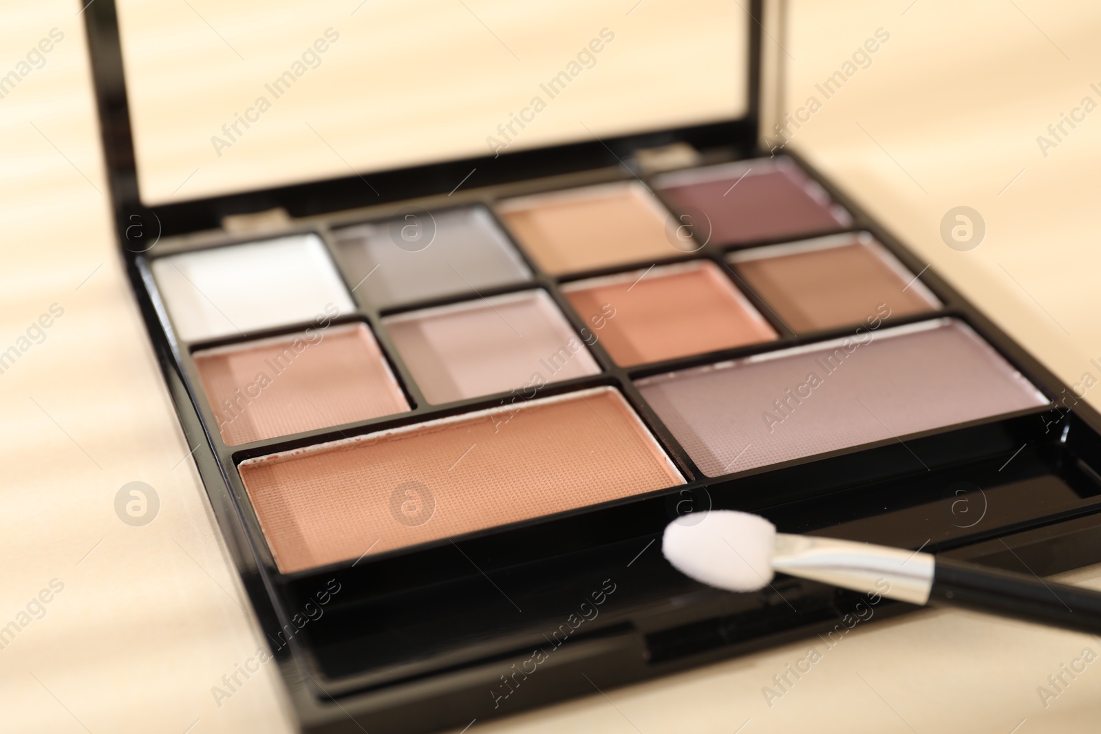 Photo of Eyeshadow palette and applicator on beige background with shadows, closeup