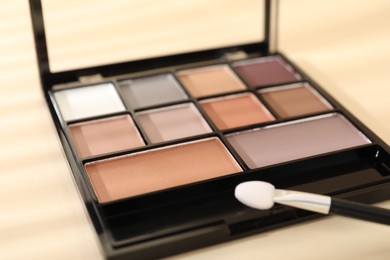 Photo of Eyeshadow palette and applicator on beige background with shadows, closeup