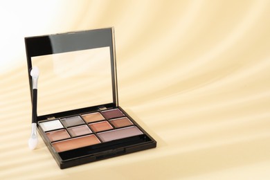 Photo of Eyeshadow palette and applicator on beige background with shadows, closeup. Space for text