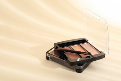 Photo of Eyeshadow palettes and mascara brush on beige background with shadows, closeup. Space for text