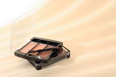 Photo of Eyeshadow palettes and mascara brush on beige background with shadows, closeup. Space for text