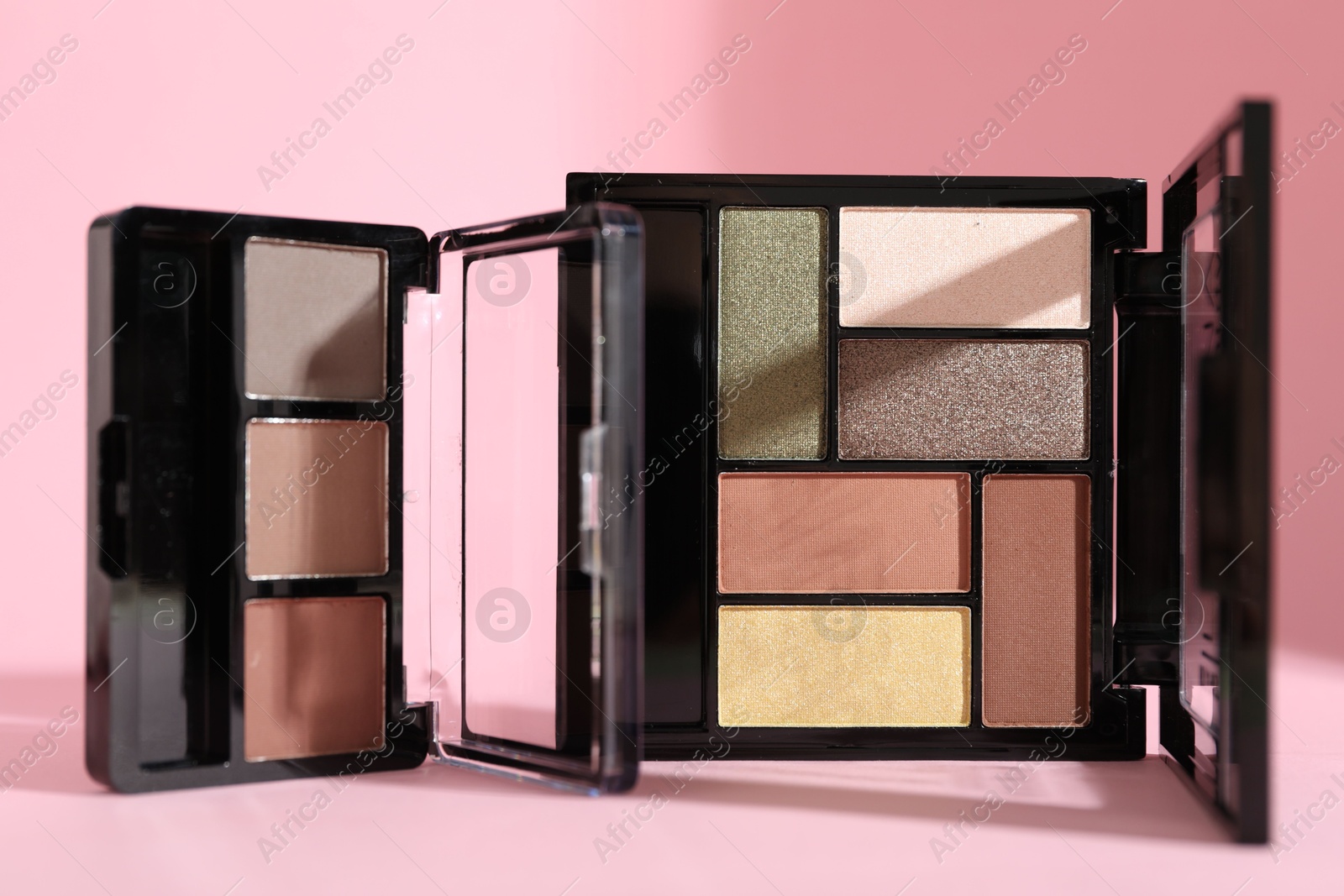Photo of Colorful eyeshadow palettes on pink background with shadows, closeup