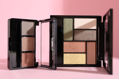 Photo of Colorful eyeshadow palettes on pink background with shadows, closeup
