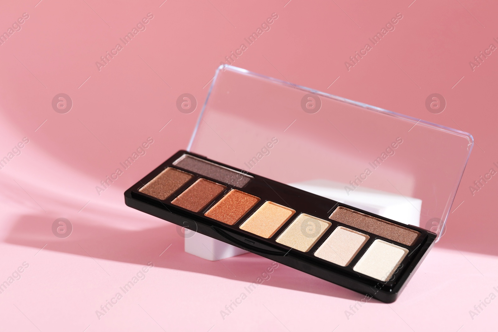 Photo of Colorful eyeshadow palette on pink background with shadows, closeup