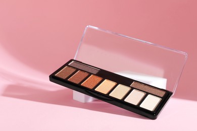 Photo of Colorful eyeshadow palette on pink background with shadows, closeup