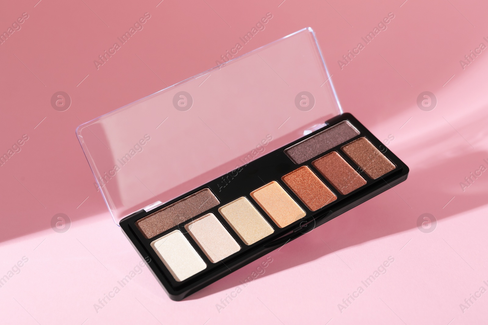 Photo of Colorful eyeshadow palette on pink background with shadows, closeup