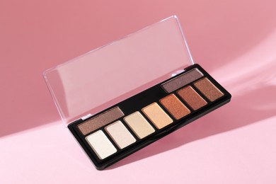 Photo of Colorful eyeshadow palette on pink background with shadows, closeup