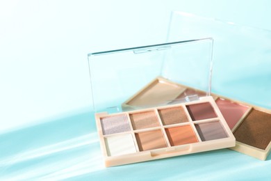 Photo of Colorful eyeshadow palettes on turquoise background, closeup. Space for text