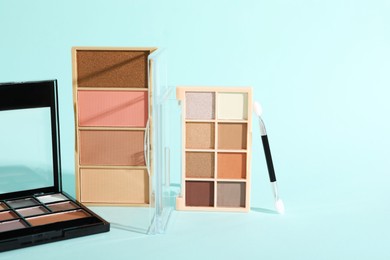 Photo of Colorful eyeshadow palettes and applicator on turquoise background, closeup. Space for text