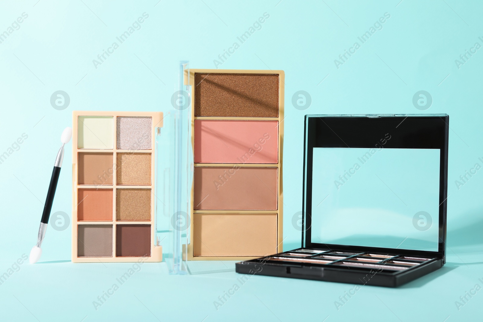 Photo of Colorful eyeshadow palettes and applicator on turquoise background, closeup