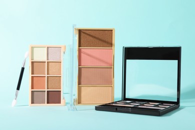 Photo of Colorful eyeshadow palettes and applicator on turquoise background, closeup