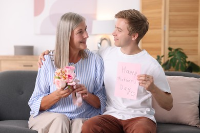 Photo of Happy Mother's Day. Son greeting his mom with bouquet of flowers and card at home