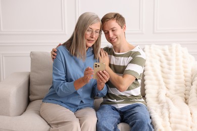 Photo of Happy son and his mother using smartphone on sofa at home