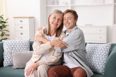 Photo of Happy son and his mother hugging on sofa at home