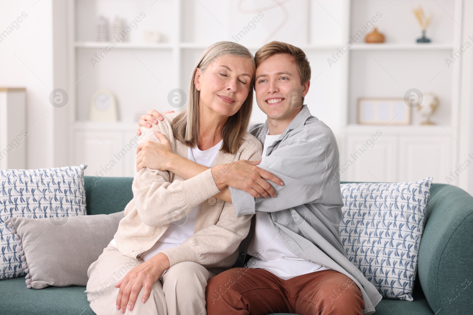Photo of Happy son and his mother hugging on sofa at home