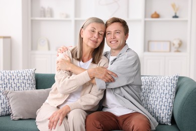 Photo of Happy son and his mother hugging on sofa at home