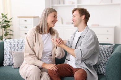 Photo of Happy son and his mother holding hands on sofa at home