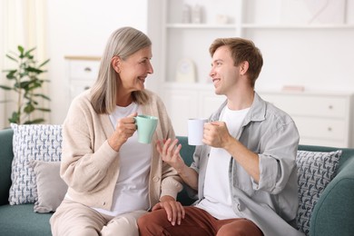 Photo of Happy son and his mother with cups spending time together on sofa at home