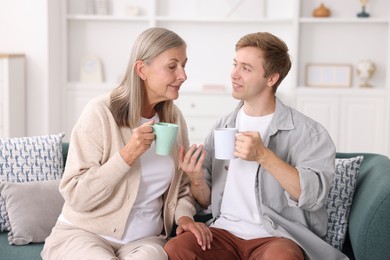 Photo of Happy son and his mother with cups spending time together on sofa at home