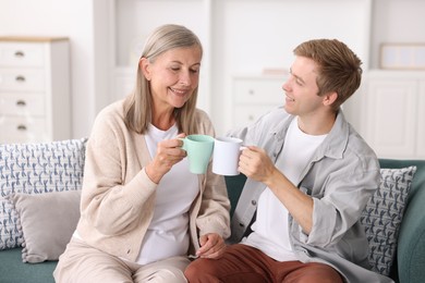 Photo of Happy son and his mother with cups spending time together on sofa at home