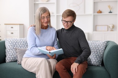 Photo of Mother and her son in glasses reading book on sofa at home
