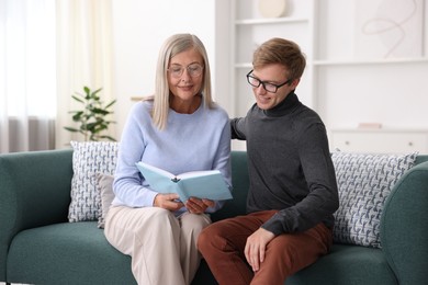 Photo of Mother and her son in glasses reading book on sofa at home