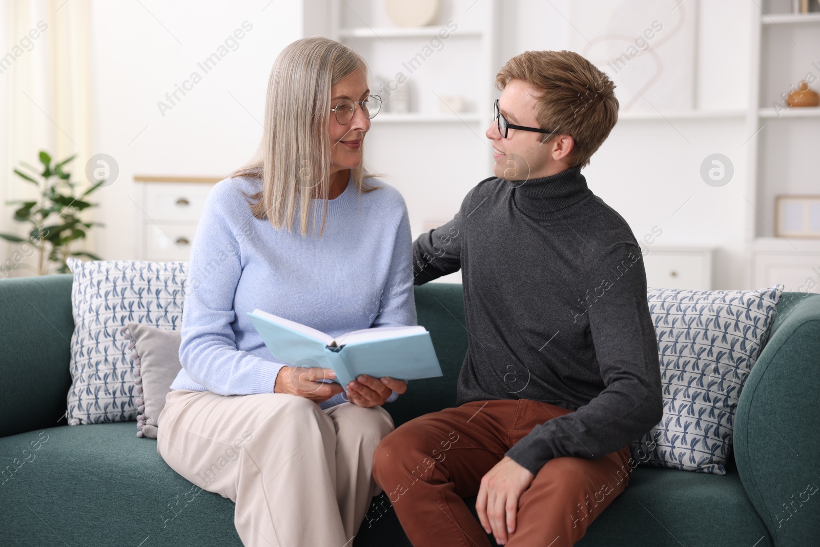 Photo of Mother and her son in glasses reading book on sofa at home