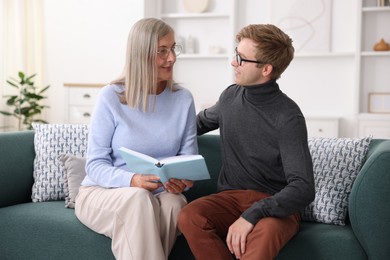 Photo of Mother and her son in glasses reading book on sofa at home