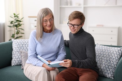 Photo of Smiling mother and her son in glasses reading book on sofa at home