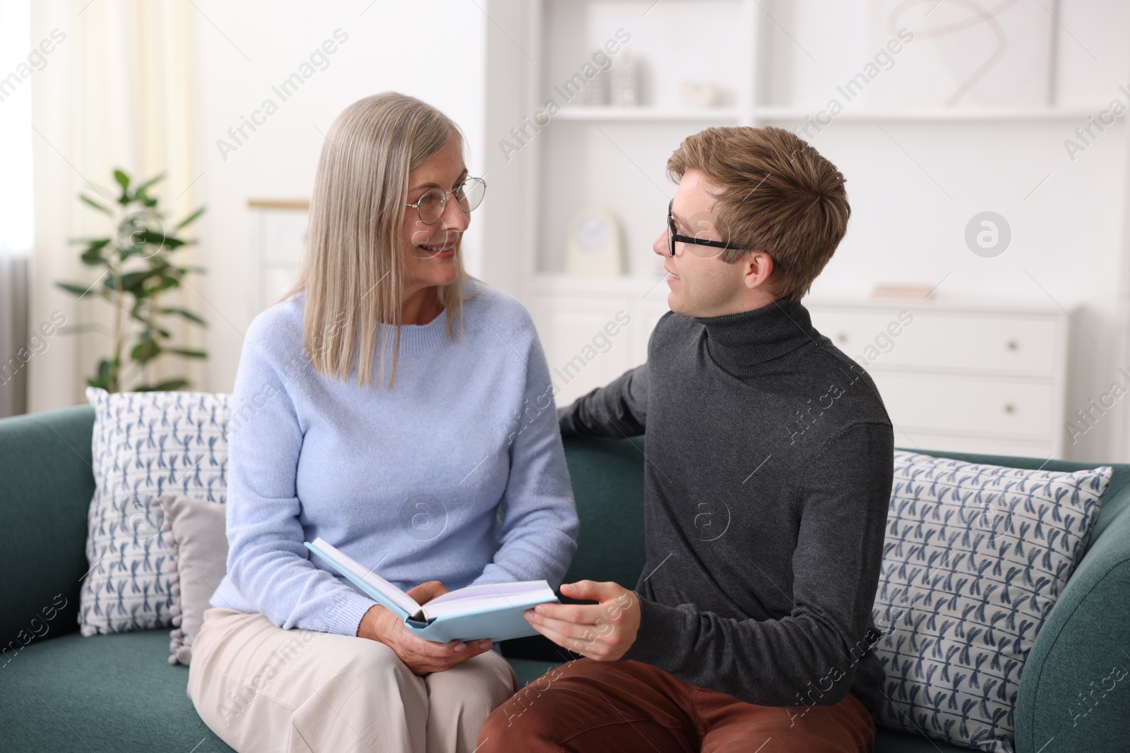 Photo of Smiling mother and her son in glasses reading book on sofa at home