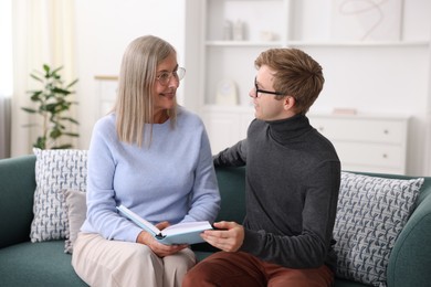 Photo of Smiling mother and her son in glasses reading book on sofa at home