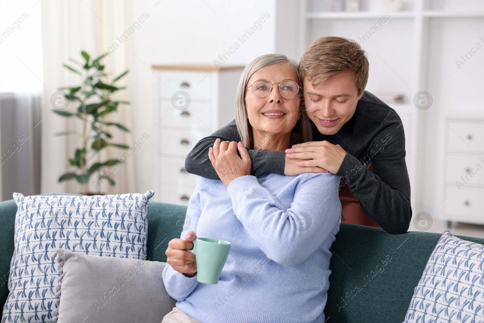 Photo of Son hugging his happy mother with cup at home