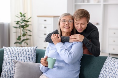 Photo of Son hugging his happy mother with cup at home