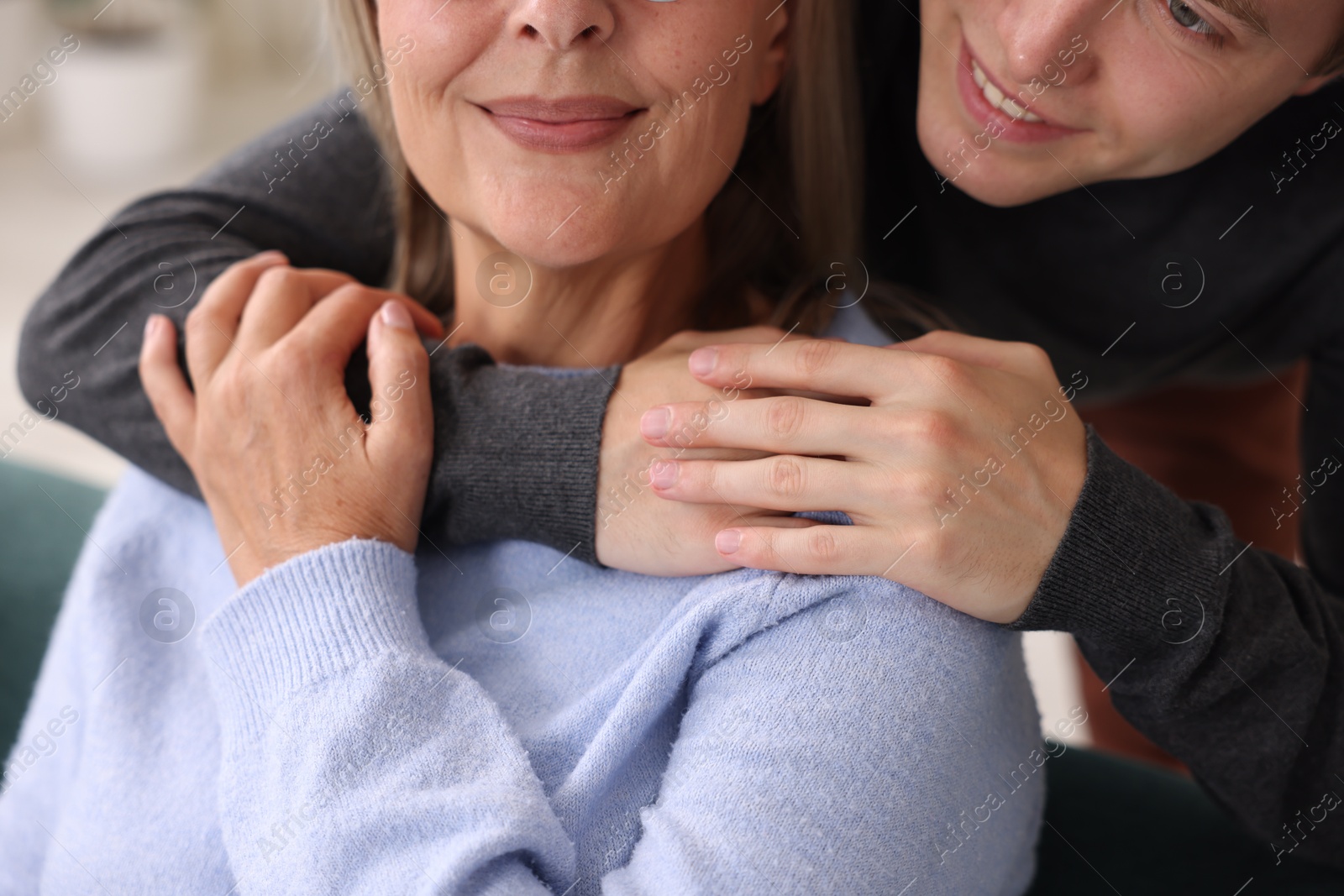 Photo of Smiling son hugging his mother indoors, closeup
